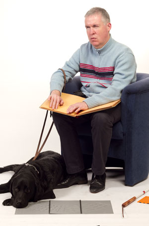 Ervaringsdeskundige. Leendert met hond, stok en braille boek.